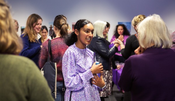 Young woman in purple shirt in conversation with older woman surrounded by a crowd at an event