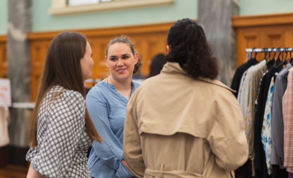 three young women stand together talking and smiling