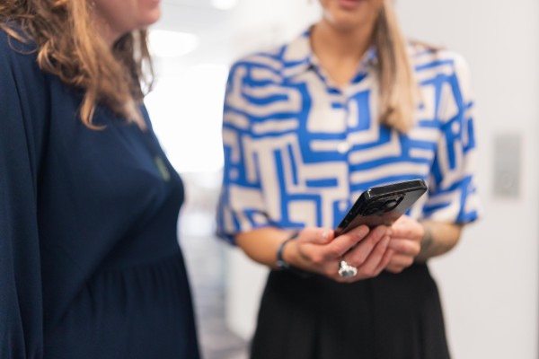 Two women stand together looking at a cellphone.