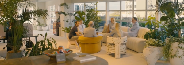A group of six people sit in a circle on multicoloured, modern shaped chairs.