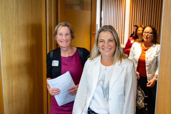 Two women look and smile at the camera while walking through a doorway.
