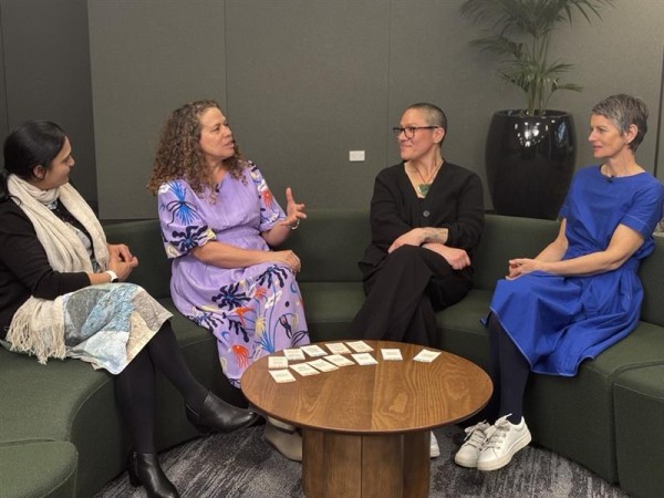 Four women sitting on a couch by a table having a discussion