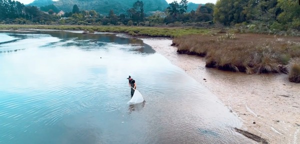 A man standing in the water at an estuary using a large hand-held net