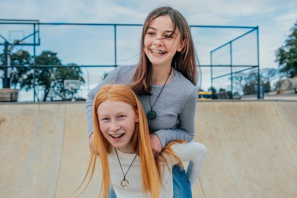 Two pre-teen girls piggybacking each other and laughing at skate park