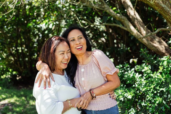 Two women in about their 30s embracing and laughing among trees
